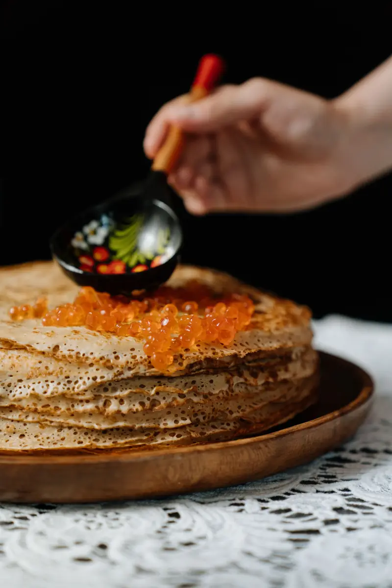 Blini topped with red caviar on a wooden plate